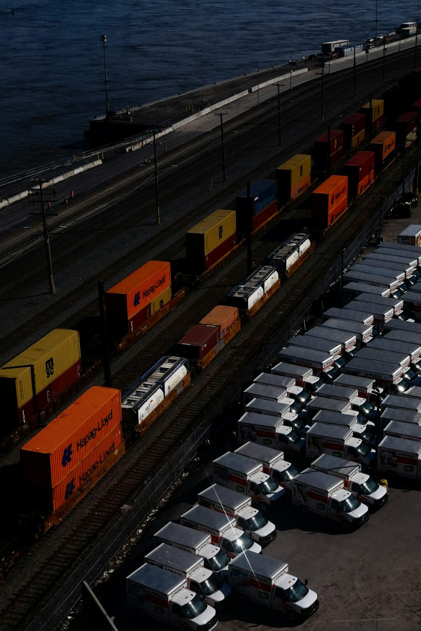 Cargo containers on rail beside a fleet of trucks at a logistics terminal.