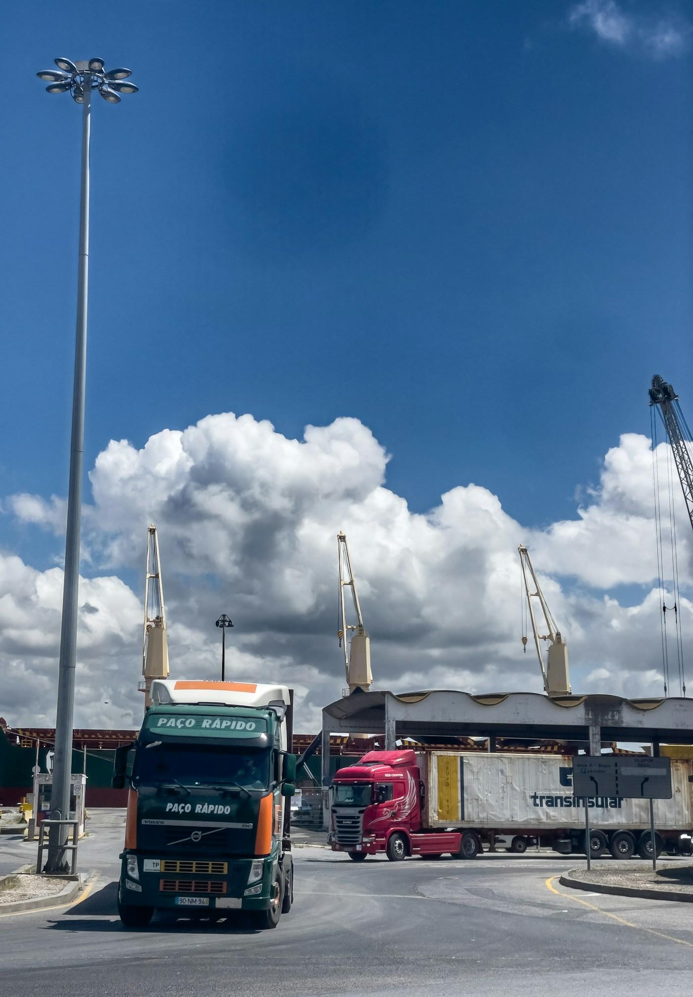 Freight trucks operating beside cranes at a shipping port.